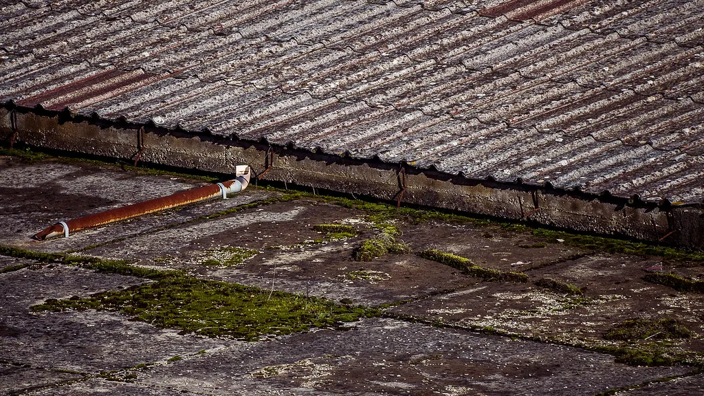 Old weathered asbestos-cement roof with moss and cracked sheets